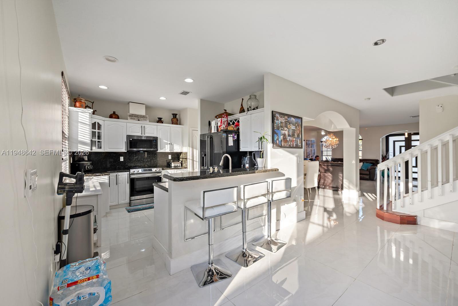 1360 Southwest 142nd Avenue Miami, FL 33184 - Photo 10 of 54 a kitchen with stainless steel appliances kitchen island granite countertop a refrigerator oven a sink a dining table and chairs with wooden floor