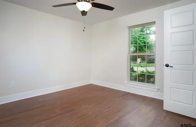 an empty room with wooden floor chandelier fan and windows