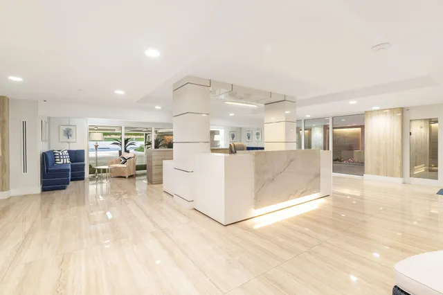 a view of a living room kitchen with stainless steel appliances kitchen island granite countertop a large window and a couch