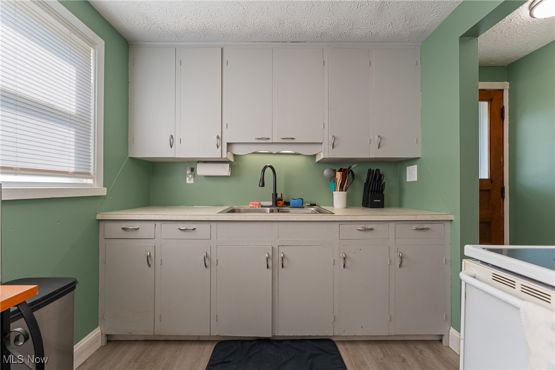 Kitchen featuring light wood-style flooring, a textured ceiling, white electric stove, and a sink