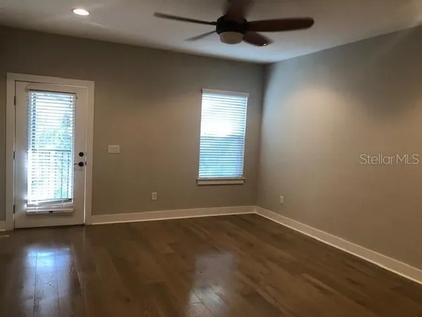an empty room with wooden floor chandelier fan and windows