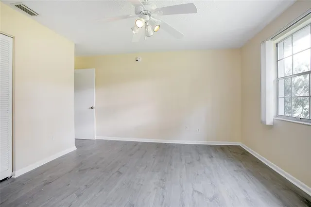 an empty room with wooden floor chandelier fan and windows