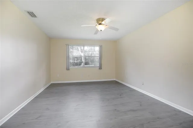 an empty room with chandelier fan and windows