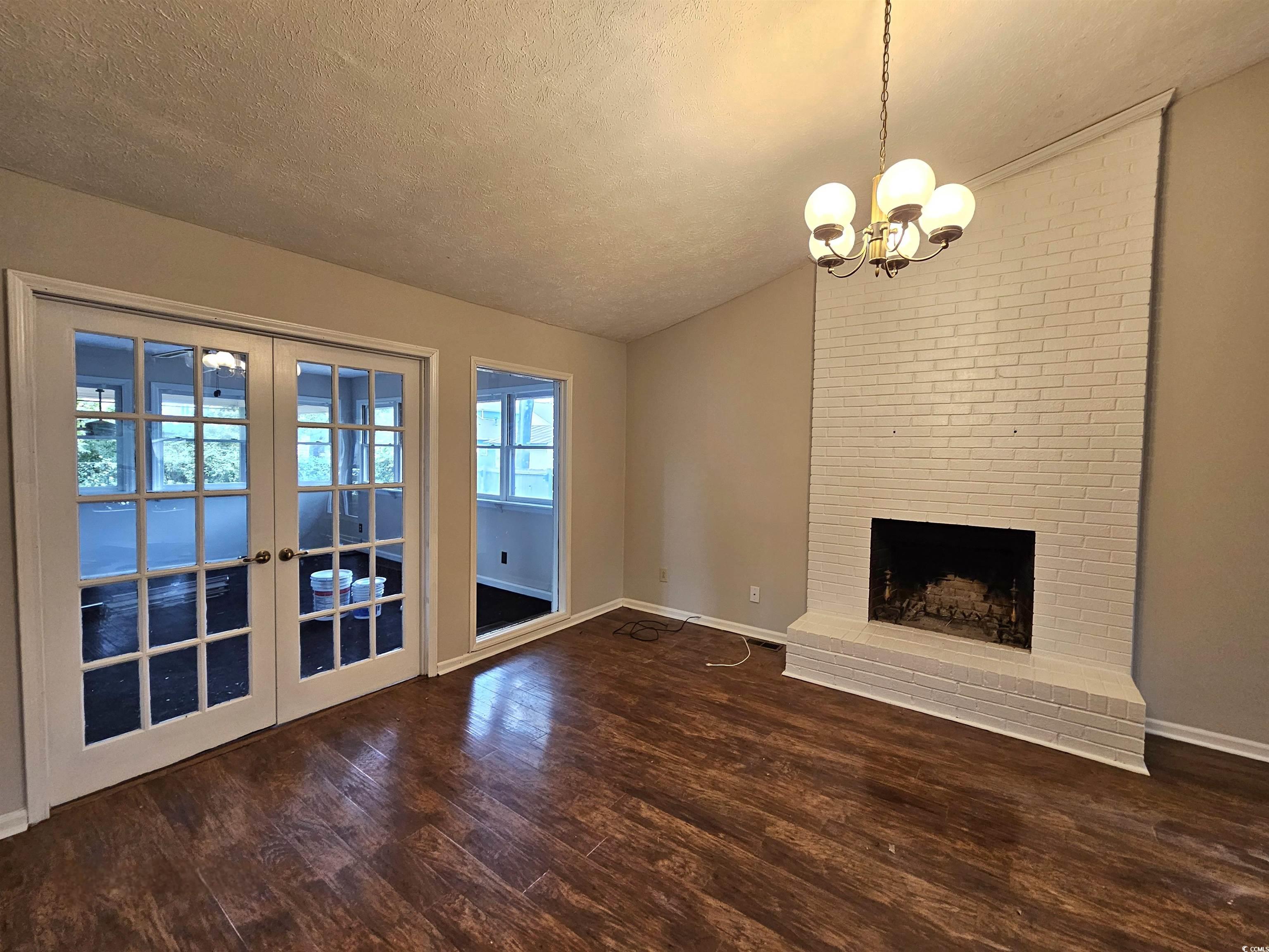 117 Partridge Berry Road Myrtle Beach, SC 29579 - Photo 11 of 33 Unfurnished living room with dark wood-style floors, lofted ceiling, a textured ceiling, a fireplace, and french doors