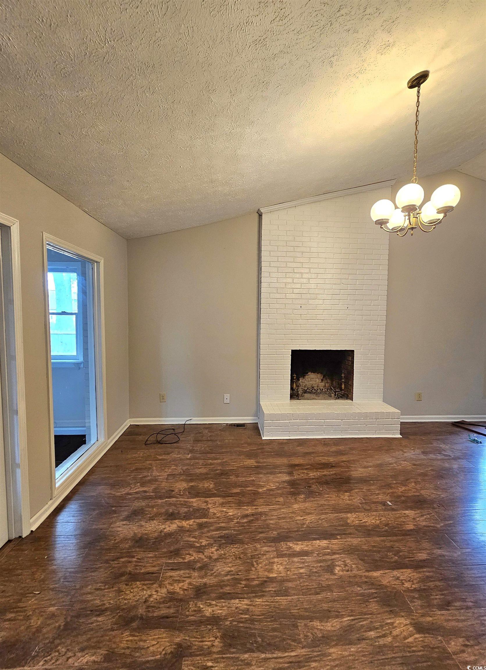 117 Partridge Berry Road Myrtle Beach, SC 29579 - Photo 12 of 33 Unfurnished living room featuring a fireplace, a textured ceiling, dark wood-type flooring, lofted ceiling, and a chandelier