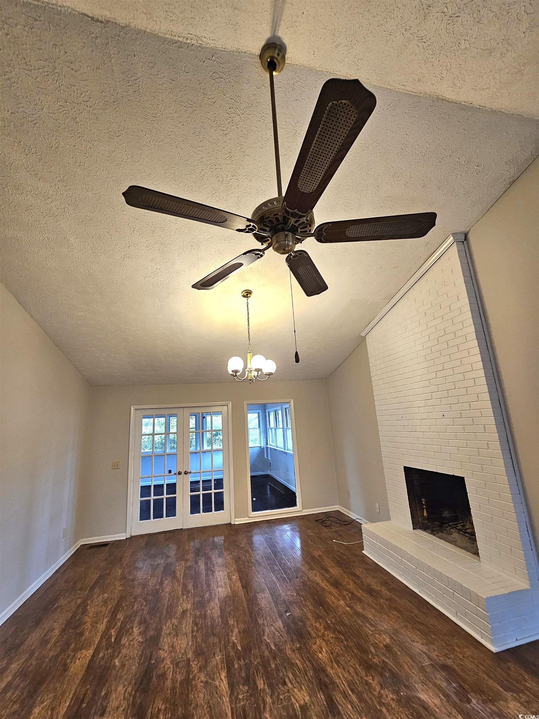 117 Partridge Berry Road Myrtle Beach, SC 29579 - Photo 13 of 33 Unfurnished living room featuring a textured ceiling, dark wood finished floors, a brick fireplace, a chandelier, and french doors