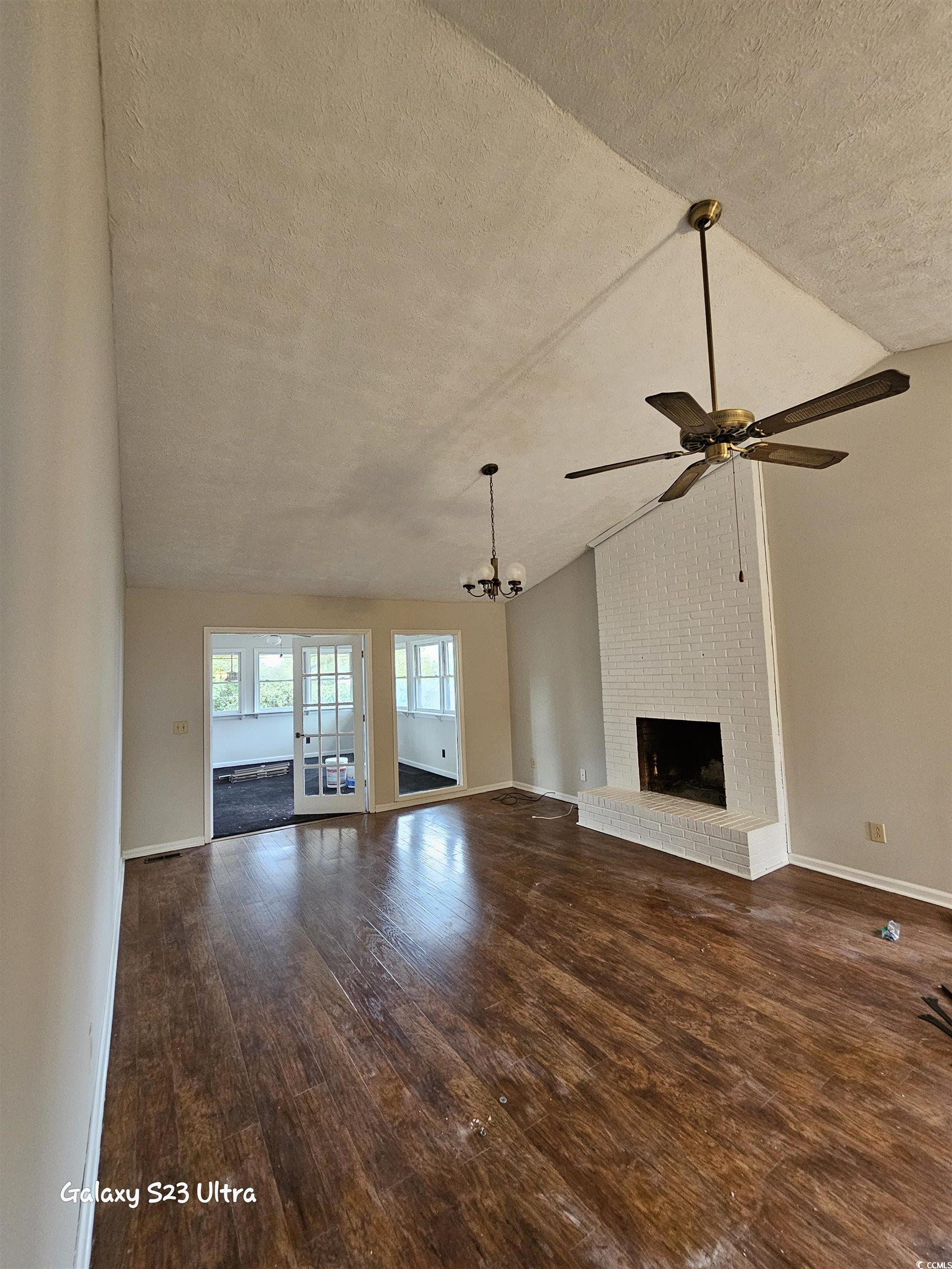 117 Partridge Berry Road Myrtle Beach, SC 29579 - Photo 10 of 33 Unfurnished living room featuring lofted ceiling, a textured ceiling, dark wood finished floors, a brick fireplace, and a chandelier
