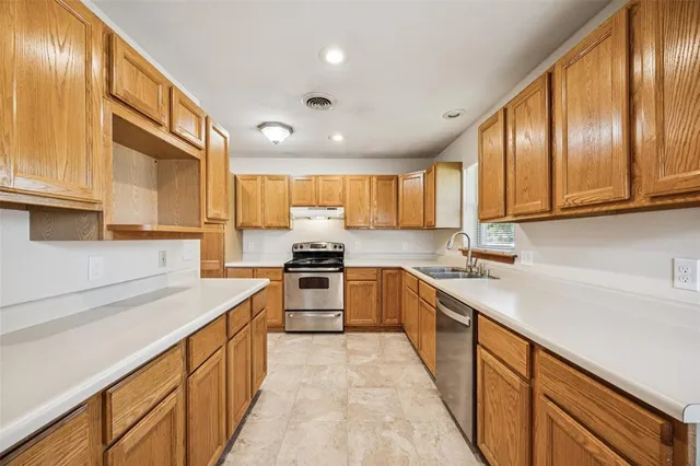 a kitchen with stainless steel appliances granite countertop a sink dishwasher stove and refrigerator with wooden cabinets