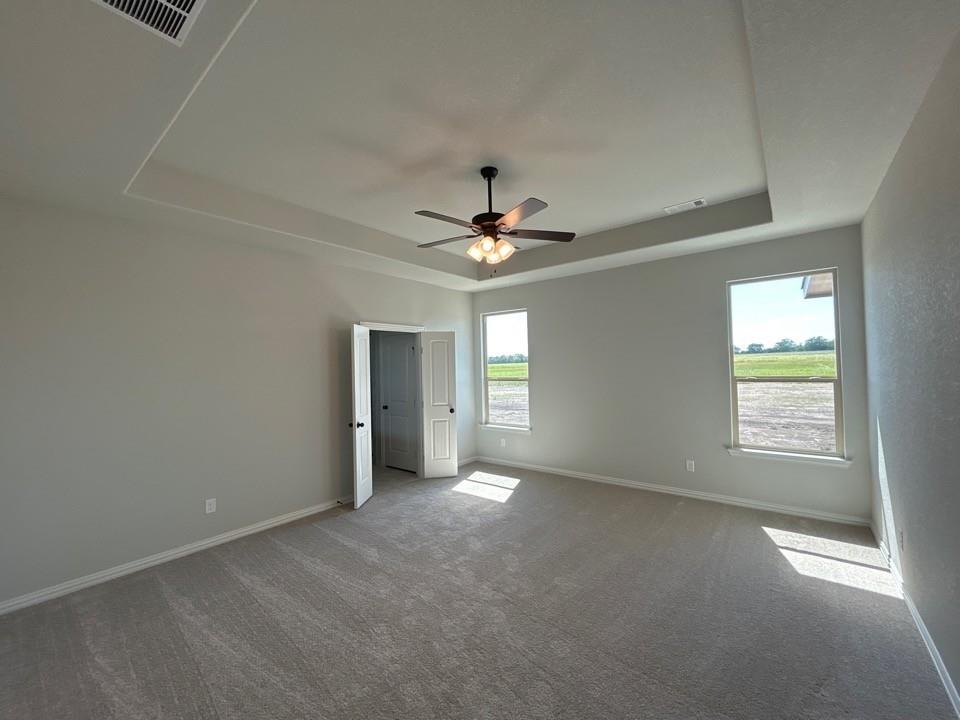 8779 County Road 623 Blue Ridge, TX 75424 - Photo 7 of 14 Spacious room featuring a tray ceiling with a ceiling fan, two windows, two paneled doors, and wall-to-wall carpeting