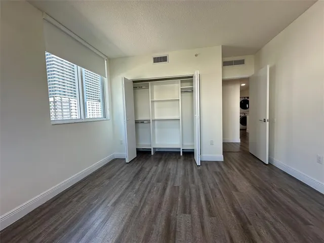 an empty room with wooden floor closet and windows