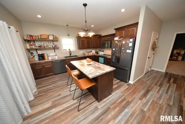 a kitchen with stainless steel appliances granite countertop a refrigerator a stove a sink dishwasher and a dining table with wooden floor