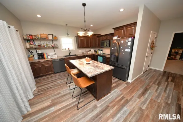 a kitchen with stainless steel appliances granite countertop a refrigerator a stove a sink dishwasher and a dining table with wooden floor