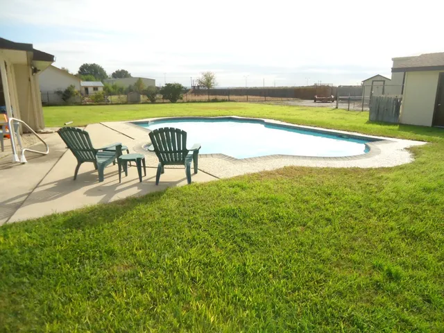 a view of a swimming pool with lawn chairs floor to ceiling window and yard