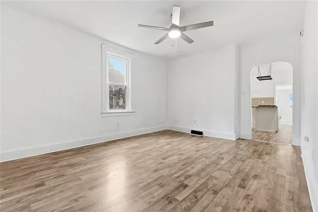 an empty room with wooden floor ceiling fan and windows
