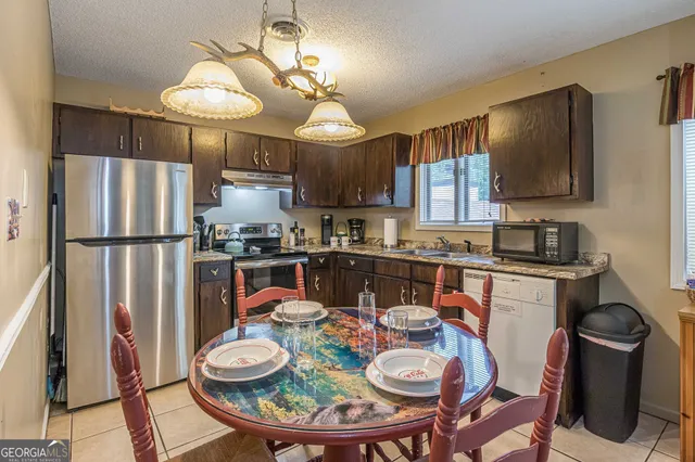 a kitchen with stainless steel appliances granite countertop a dining table and chairs a refrigerator with wooden floor