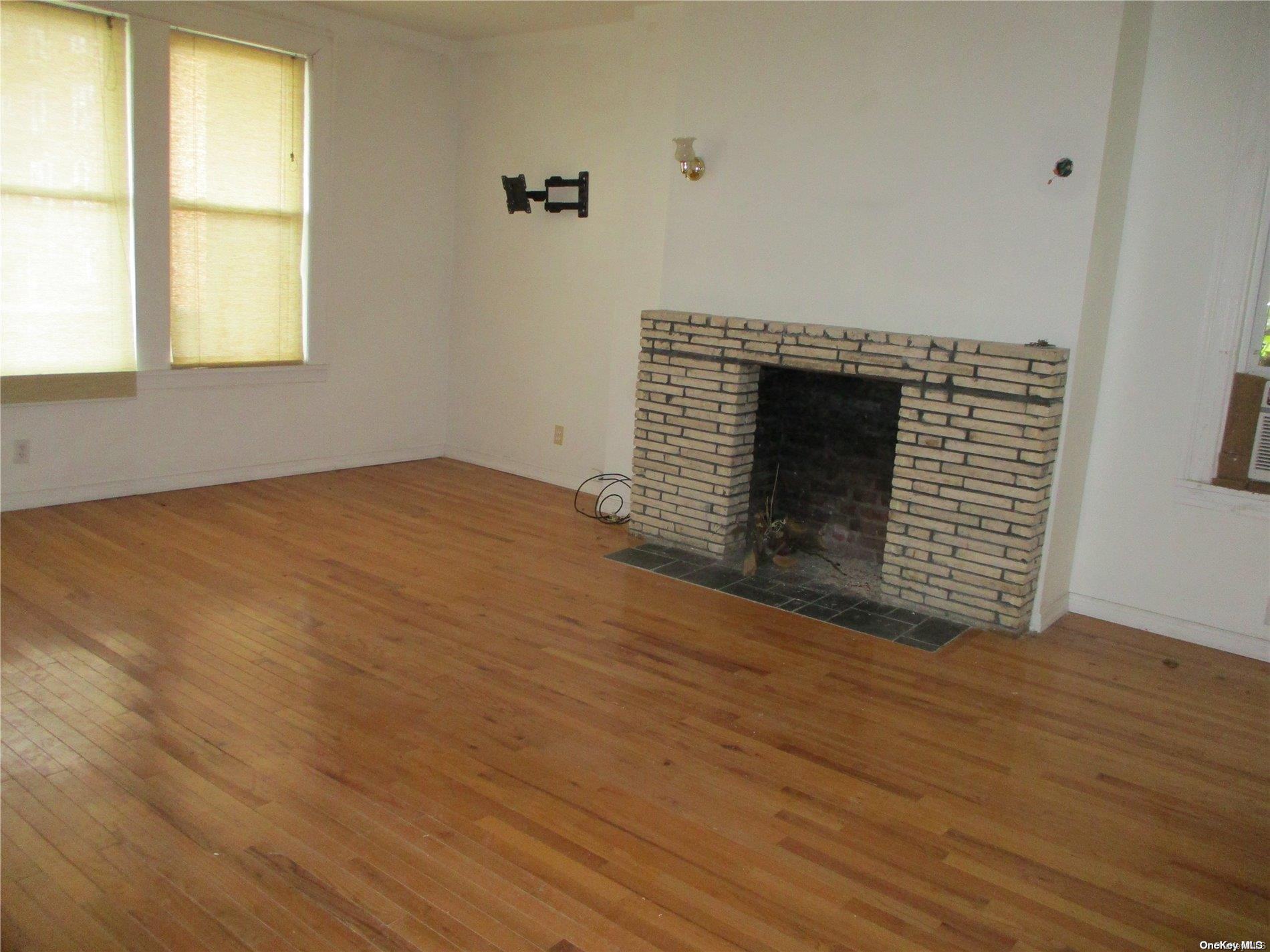 135 Beach 124th Street Queens, NY 11694 - Photo 2 of 25 an empty room with wooden floor windows and fireplace