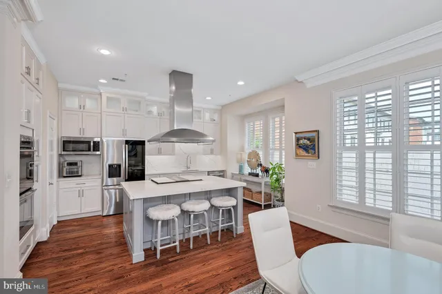 a large kitchen with stainless steel appliances kitchen island a large counter top a stove a chimney a sink and a refrigerator