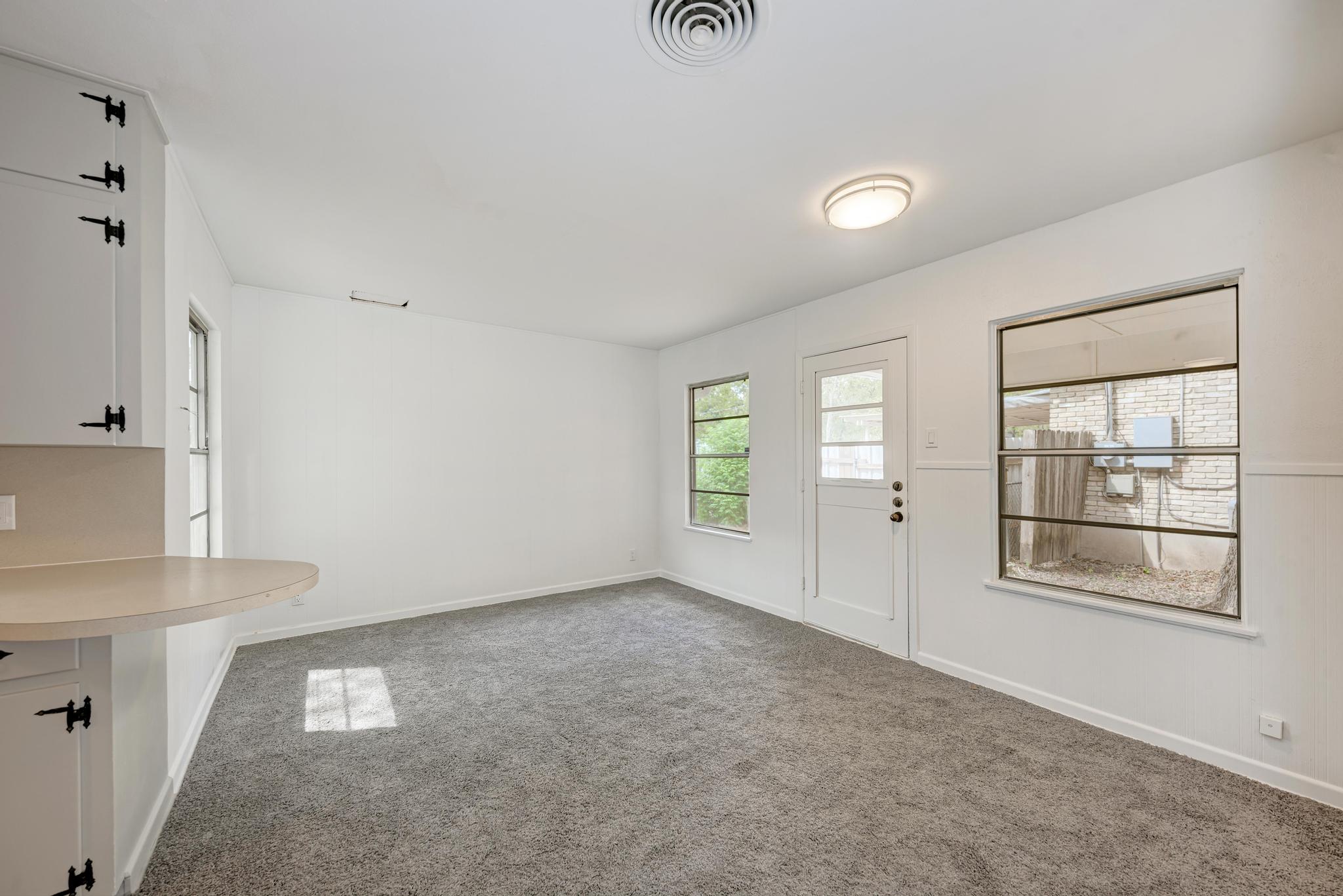 7804 Rutgers Avenue Austin, TX 78757 - Photo 5 of 32 Plentiful natural light streams across carpeted flooring through multiple windows and a glass-paneled door.