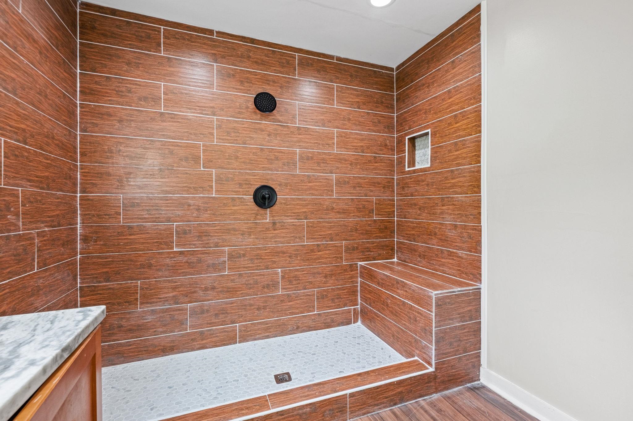 5843 Stewart Road Lakeland, TN 38002 - Photo 19 of 26 Walk-in shower featuring wood-finish wall tiling, integrated shower bench, dual matte black fixtures, recessed niche, and a white aggregate shower pan