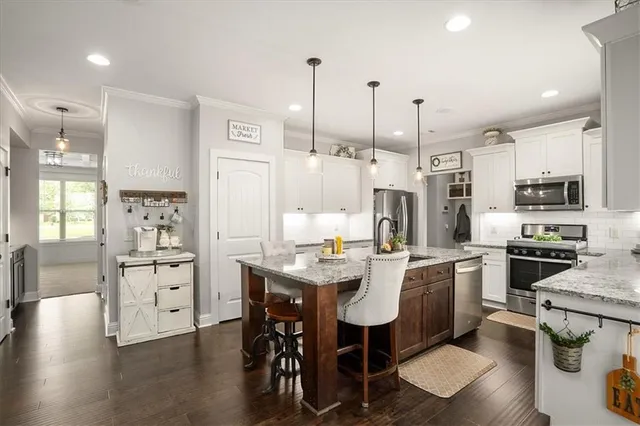 a kitchen with stainless steel appliances kitchen island granite countertop a stove a sink a refrigerator a dining table and chairs with wooden floor