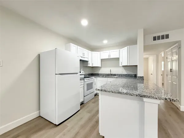 a kitchen with granite countertop a refrigerator a sink and white cabinets
