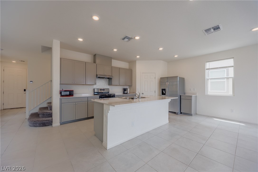 5927 Coja Street Las Vegas, NV 89113 - Photo 8 of 32 Kitchen featuring gray cabinets, appliances with stainless steel finishes, under cabinet range hood, light countertops, and an island with sink