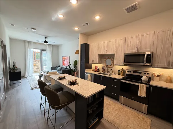 a kitchen with stainless steel appliances granite countertop a stove top oven a sink dishwasher a dining table and chairs with wooden floor