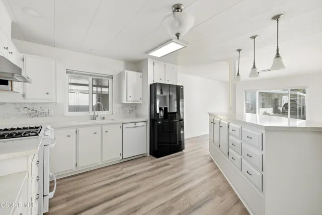 a kitchen with granite countertop a refrigerator oven a sink dishwasher and white cabinets with wooden floor