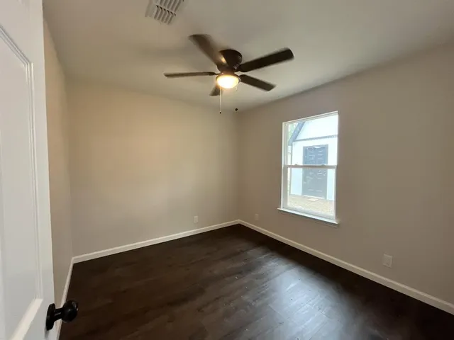 an empty room with wooden floor ceiling fan and windows