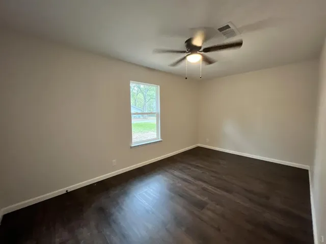 an empty room with wooden floor ceiling fan and windows
