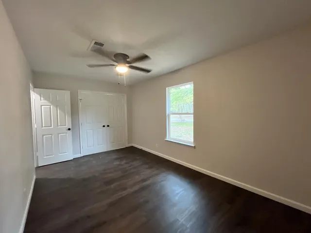 an empty room with wooden floor chandelier fan and windows