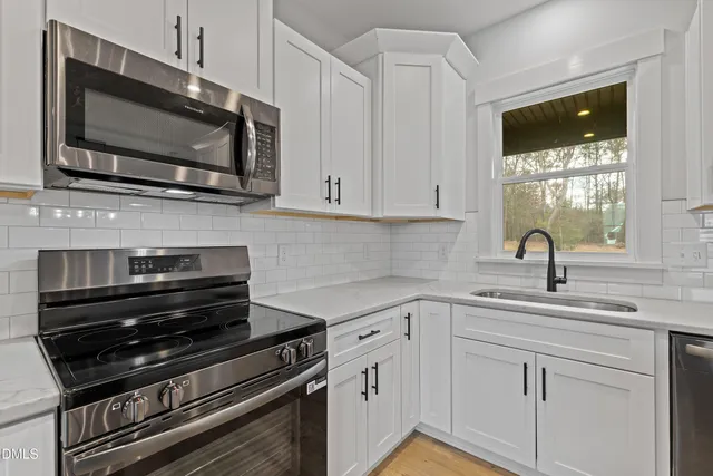 a large kitchen with granite countertop a large kitchen island a sink dishwasher a refrigerator and white cabinets with wooden floor