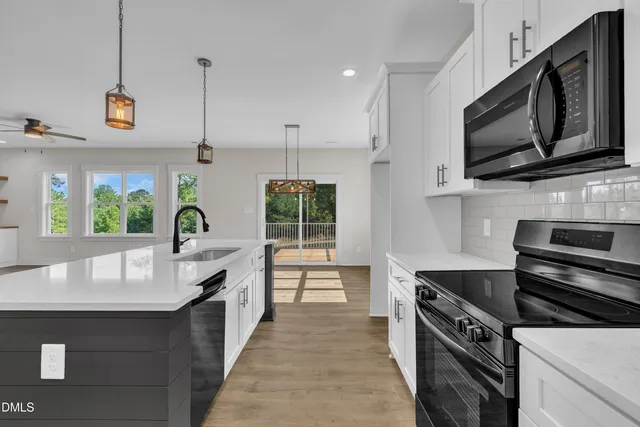 a kitchen with stainless steel appliances granite countertop a sink a microwave oven a refrigerator and white cabinets with wooden floor