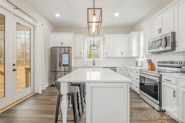 a kitchen with stainless steel appliances kitchen island granite countertop a refrigerator oven a sink dishwasher and white cabinets with wooden floor