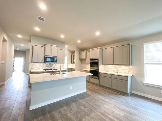 a large kitchen with kitchen island a stove a sink a refrigerator and white cabinets with wooden floor