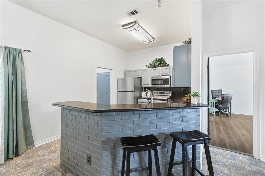 217 Seay Road Italy, TX 76651 - Photo 12 of 38 Kitchen with stainless steel appliances, a breakfast bar area, gray cabinetry, a peninsula, and dark stone counters