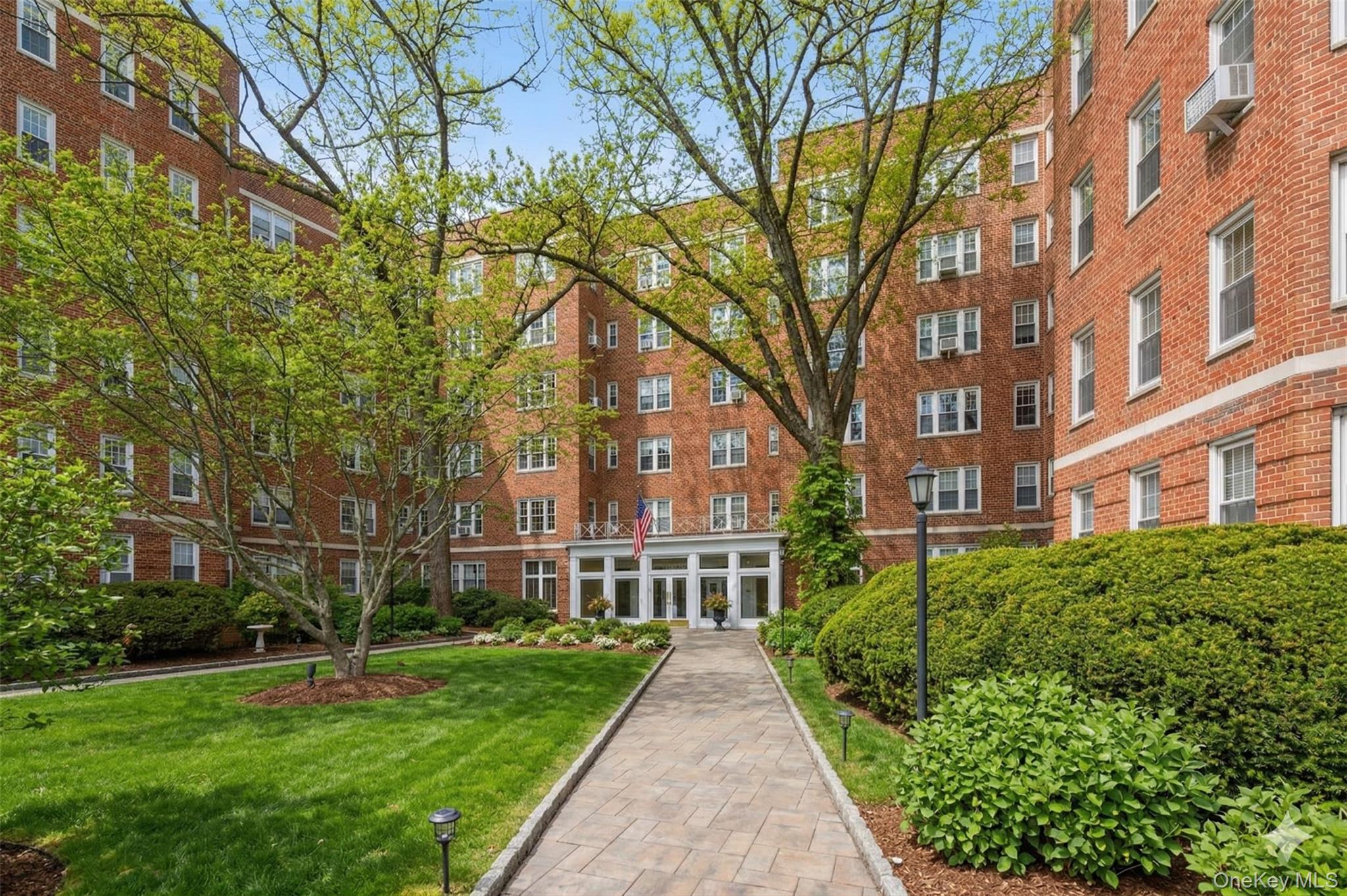 a view of a brick building next to a big yard and large trees