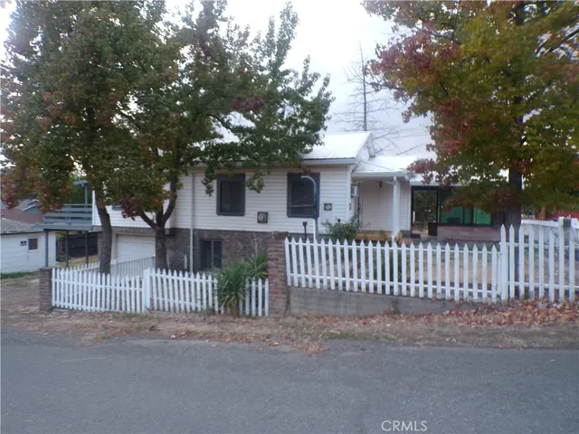 a view of a white house with a large tree and wooden fence