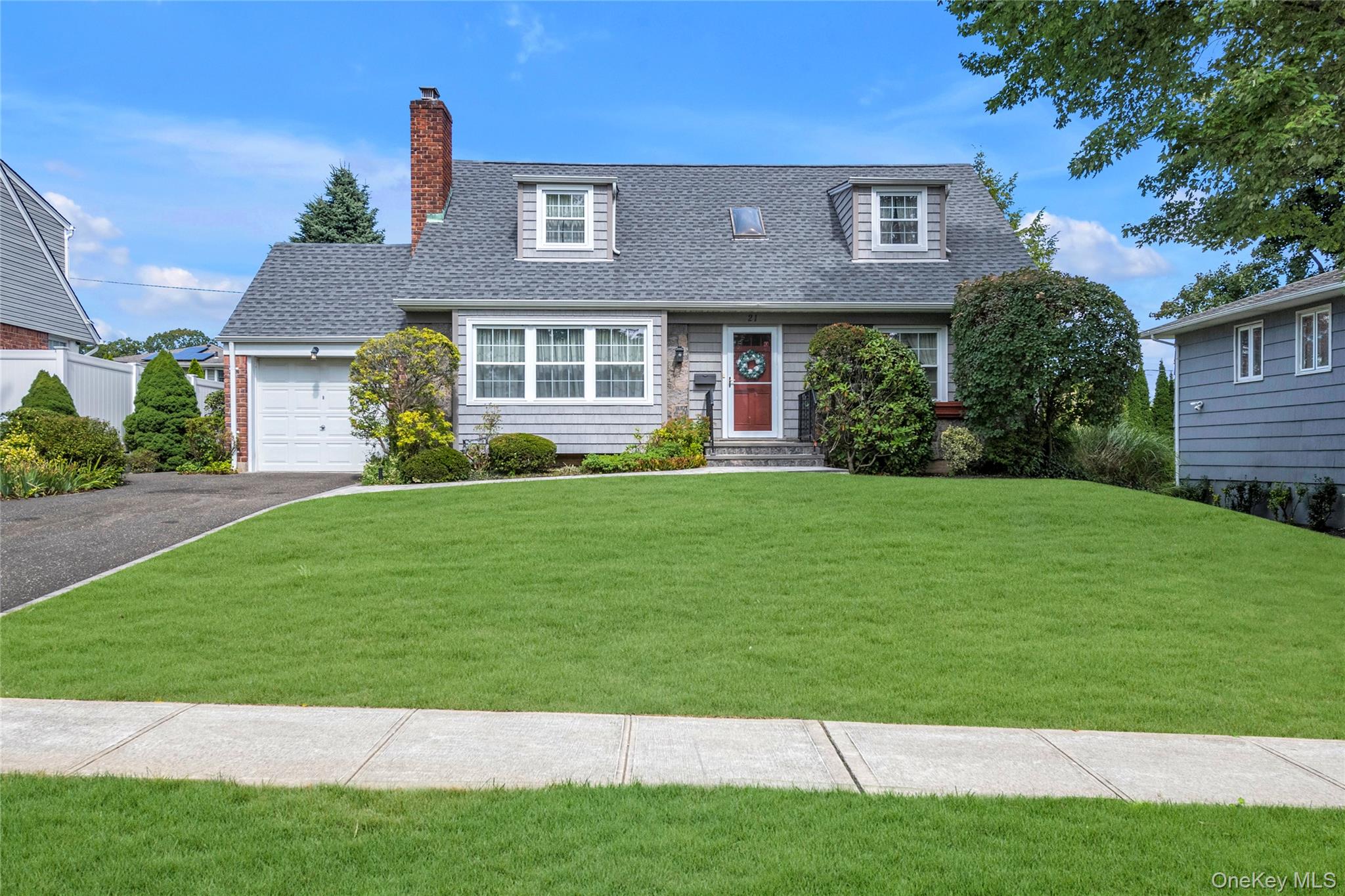 Cape cod house with a shingled roof, a front lawn, an attached garage, driveway, and a chimney