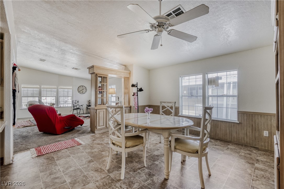 4552 Royal Ridge Avenue Las Vegas, NV 89103 - Photo 5 of 13 Dining room featuring a wainscoted wall, a textured ceiling, wooden walls, healthy amount of natural light, and a ceiling fan