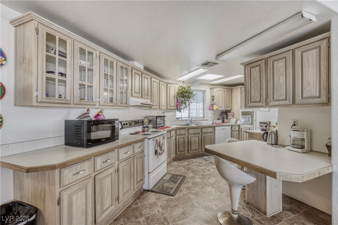 4552 Royal Ridge Avenue Las Vegas, NV 89103 - Photo 7 of 13 Kitchen featuring light countertops, a breakfast bar, glass insert cabinets, white appliances, and a peninsula