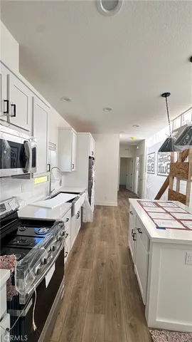 a kitchen with stainless steel appliances a stove a sink dishwasher a refrigerator and white cabinets with wooden floor