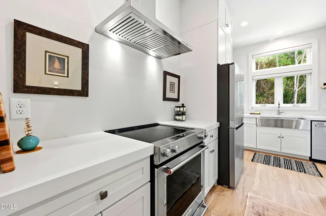 a kitchen with stainless steel appliances white cabinets a stove a sink and a window