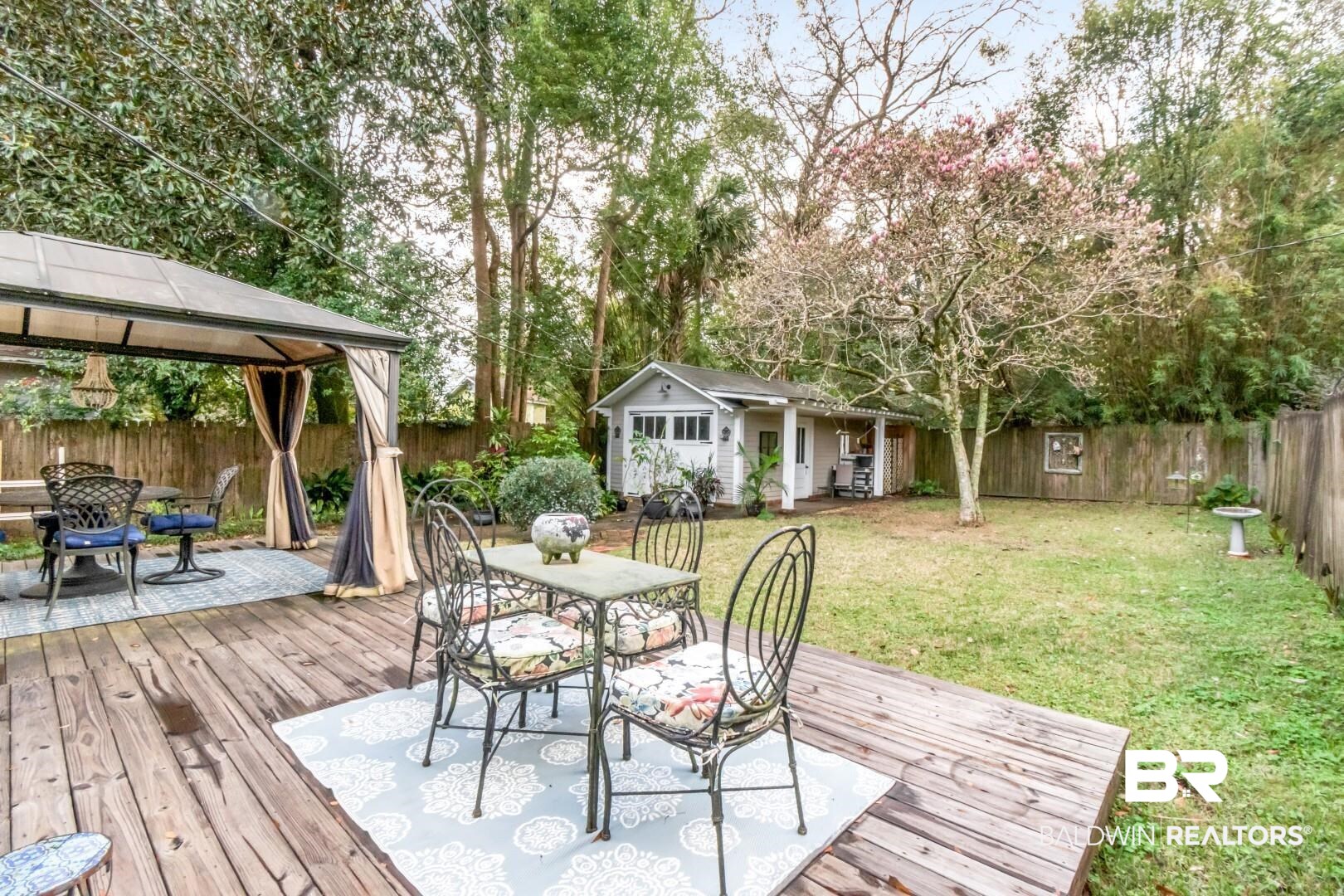 135 Silverwood Street Mobile, AL 36607 - Photo 21 of 32 Wooden deck featuring outdoor dining space, an outbuilding, a fenced backyard, a gazebo, and view of wooded area