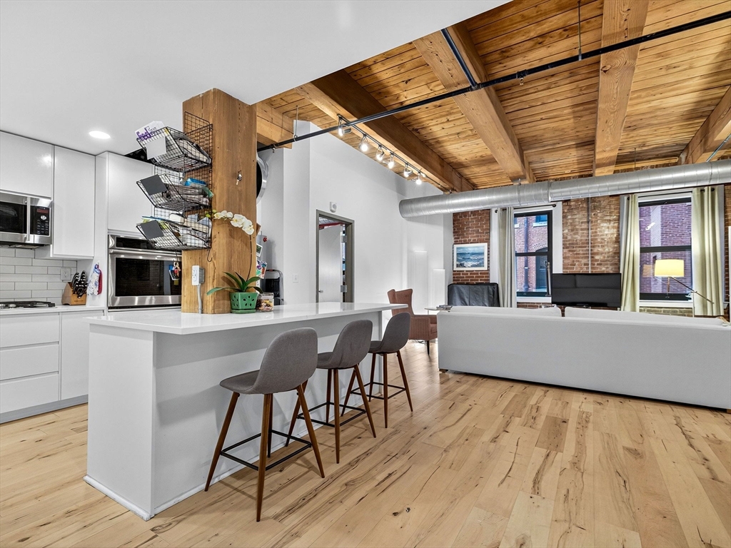 a living room with stainless steel appliances kitchen island granite countertop a table chairs sink and wooden floor