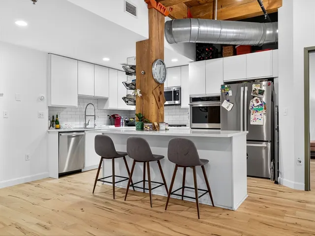 a kitchen with stainless steel appliances kitchen island granite countertop a refrigerator a stove and white cabinets with wooden floor