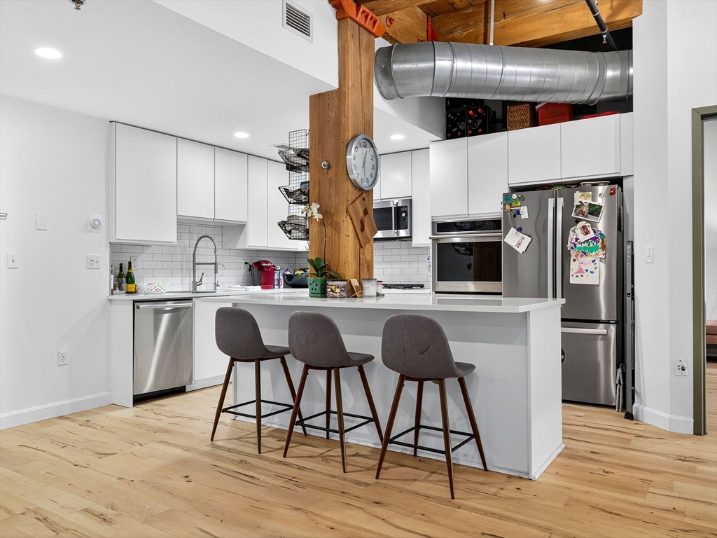 9 West Broadway, Unit 206 Boston, MA 02127 - Photo 2 of 25 a kitchen with stainless steel appliances kitchen island granite countertop a refrigerator a stove and white cabinets with wooden floor