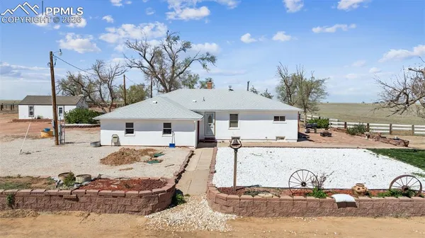 a view of a white house next to a yard with big trees