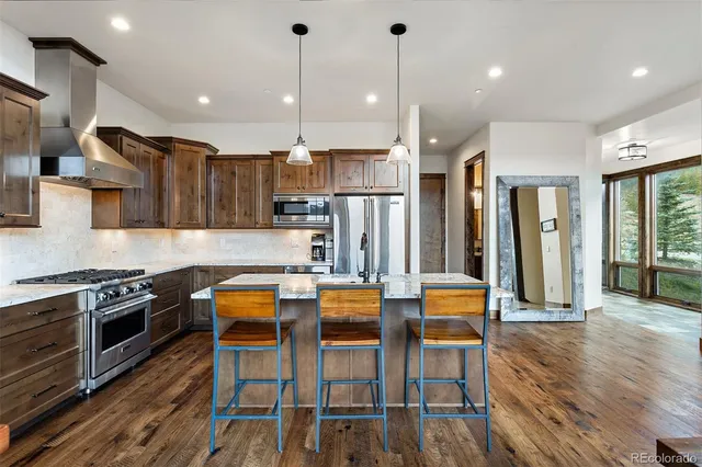 a kitchen with stainless steel appliances granite countertop a stove a refrigerator a oven a sink with island a dining table and chairs