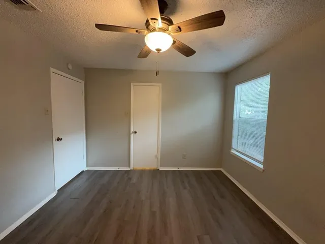 an empty room with wooden floor fan and window